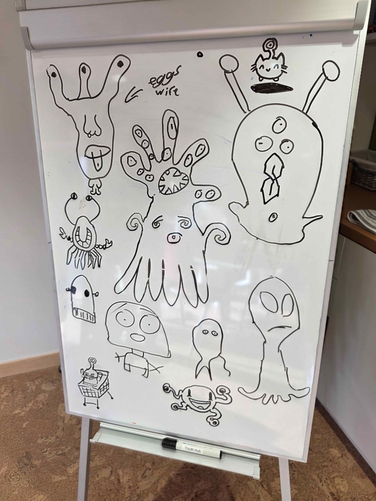 Whiteboard filled with hand-drawn monster character sketches.